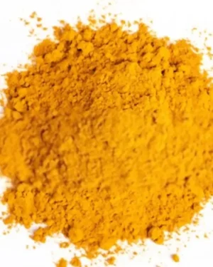 A mound of bright orange-yellow Turmeric powder is spread on a plain white background. The texture of the organic spice is fine and slightly uneven, with small clumps and loose granules scattered around the central pile.
