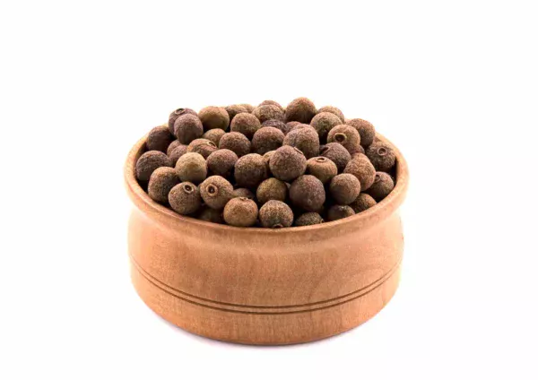 A wooden bowl filled with Allspice, displayed against a white background. The whole organic allspice berries are small, round, and have a brown color with a slightly coarse texture.