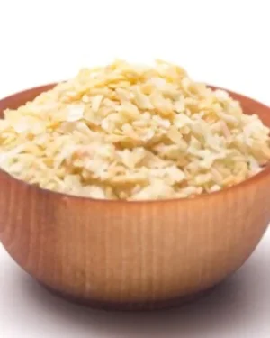 A wooden bowl filled to the brim with shredded dehydrated onion from Heil Herbs Co. The bowl is set against a plain white background. The texture of the onion flakes is rough and appears light cream in color.