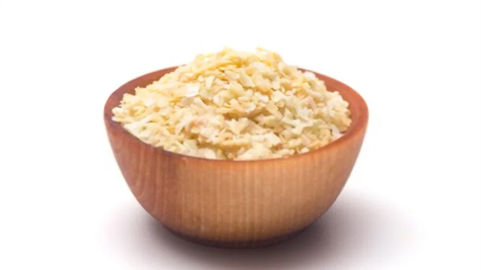 A wooden bowl filled to the brim with shredded dehydrated onion from Heil Herbs Co. The bowl is set against a plain white background. The texture of the onion flakes is rough and appears light cream in color.