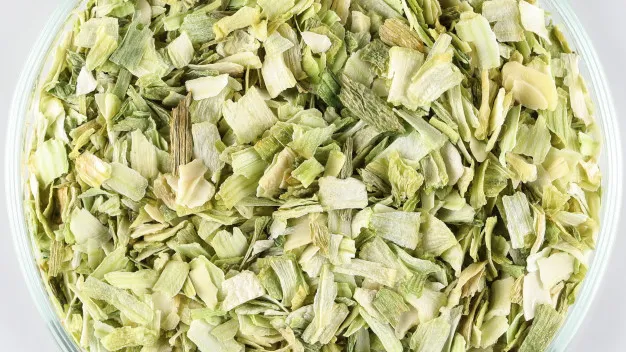 A close-up image of a bowl filled with dried, chopped premium quality Leek. The Leek pieces are in varying shades of green and white, showcasing their dehydrated texture. The small, irregularly shaped pieces hint at their use in cooking or seasoning.