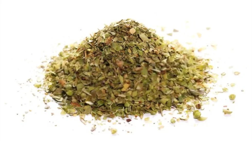 A pile of dried Oregano, finely chopped, is placed on a white background. The green and brown leaves are loosely scattered, showcasing their texture and colors—an excellent sample from our bulk supplier specializing in Egyptian Oregano.