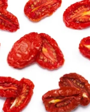 A scattering of Dried Tomatoes in various shapes and sizes on a white background. The deeply red, wrinkled pieces, some halved to reveal their seeds and inner texture, illustrate the quality offered by a top supplier of Dried Tomatoes.