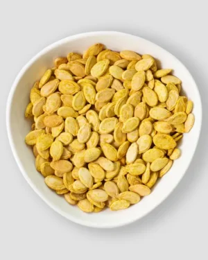 A bowl brimming with Pumpkin Seeds rests against a simple light gray backdrop. The roasted organic seeds, golden brown from perfect seasoning and cooking, are sourced from a renowned Egyptian supplier, promising both health benefits and delicious flavor.
